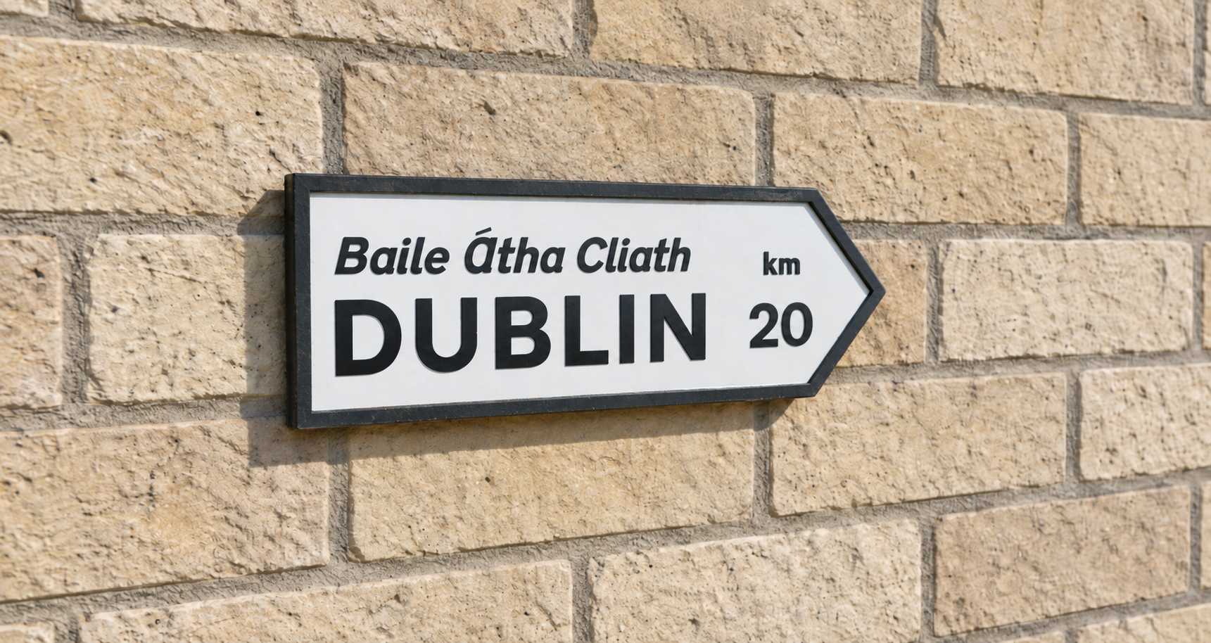 Bilingual Baile Átha Cliath and Dublin direction sign mounted on a pale stone wall